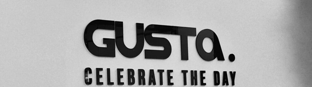 Schwarzes Acrylglas-Logo 'Gusta' auf weißer Wand, hergestellt von Birse. Buchstaben 3D.