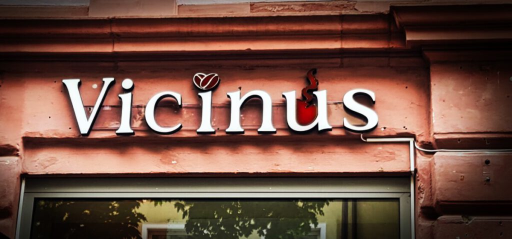 Elegante LED-Leuchtbuchstaben 'Vicinus' mit einem Kaffeebohnen-Symbol an einer Gebäudefassade.